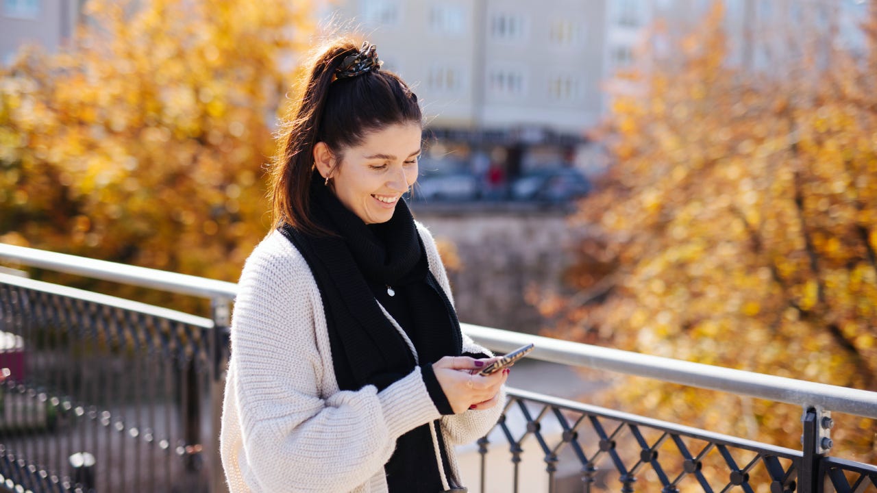 Woman smiling at cellphone in fall weather