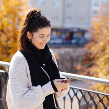 Woman smiling at cellphone in fall weather