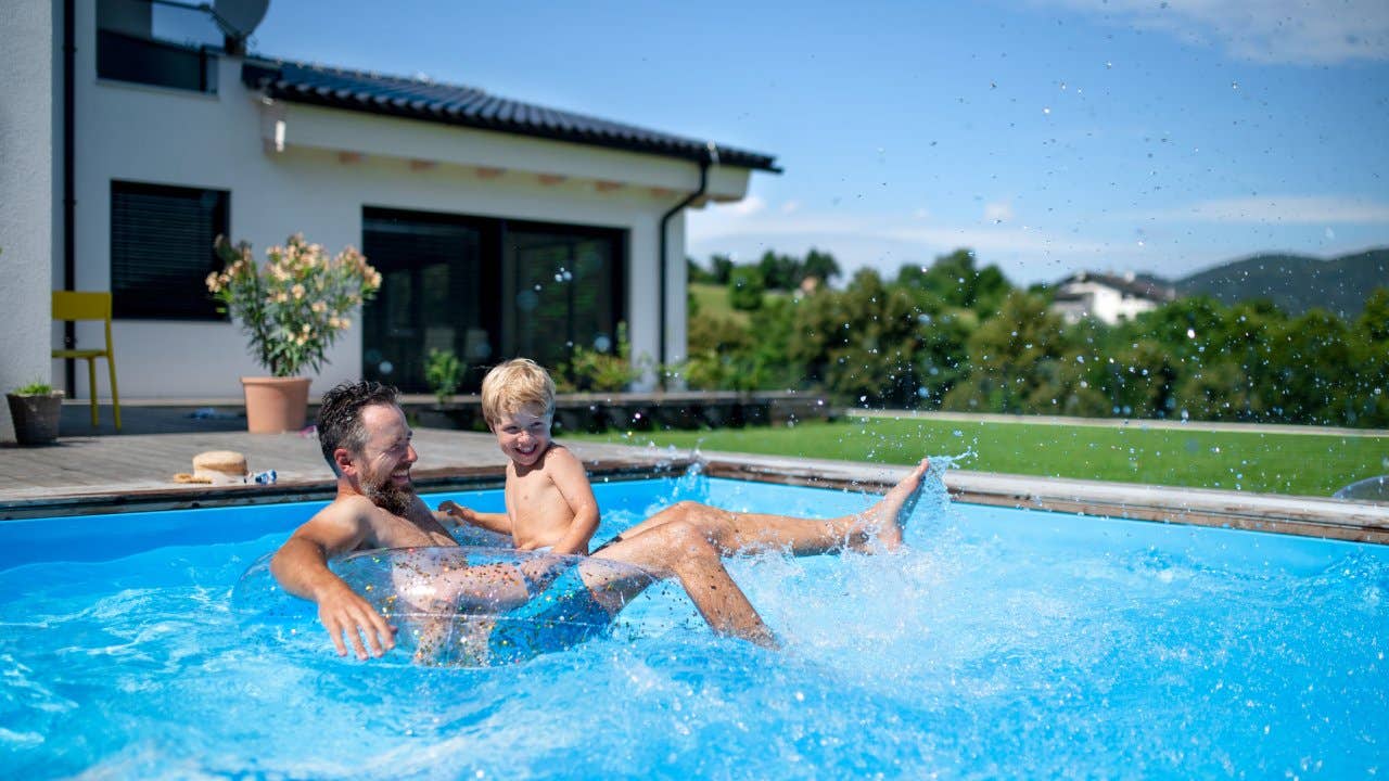 Father with small son playing in swimming pool in backyard.