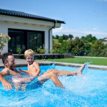 Father with small son playing in swimming pool in backyard.