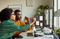A Black couple looks at a pair of computer screens together.