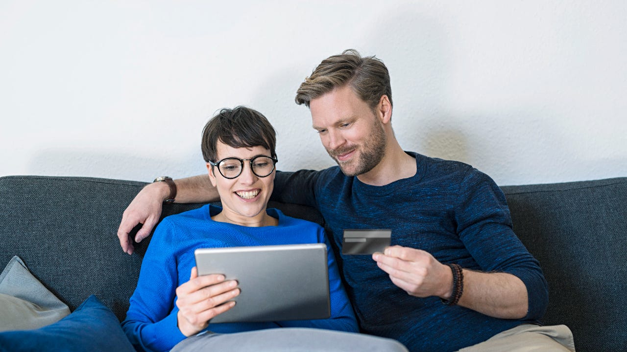 Happy casual couple relaxing on couch using tablet and holding credit card