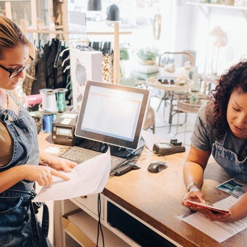 Colleagues discussing over financial receipt with digital tablet at checkout counter in store