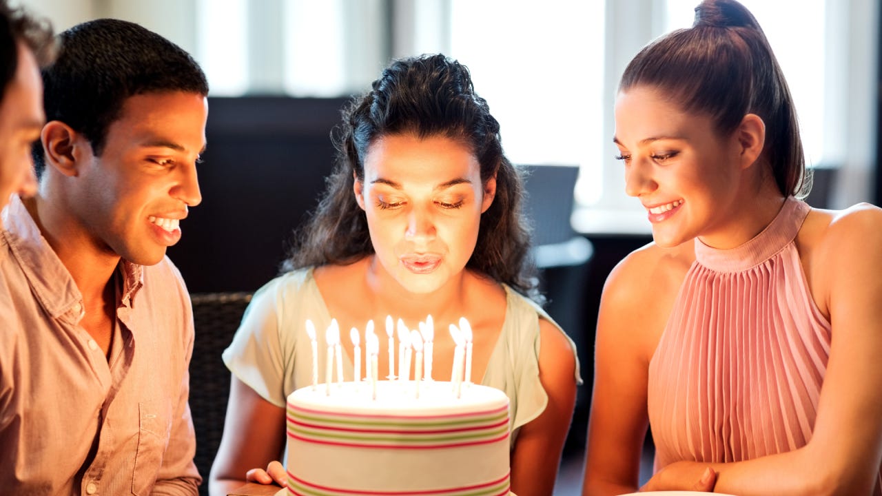 Young woman blowing birthday candles while friends looking at it in restaurant. Horizontal shot.