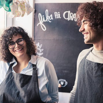 Male and female co-owners work together in aprons at a shop.