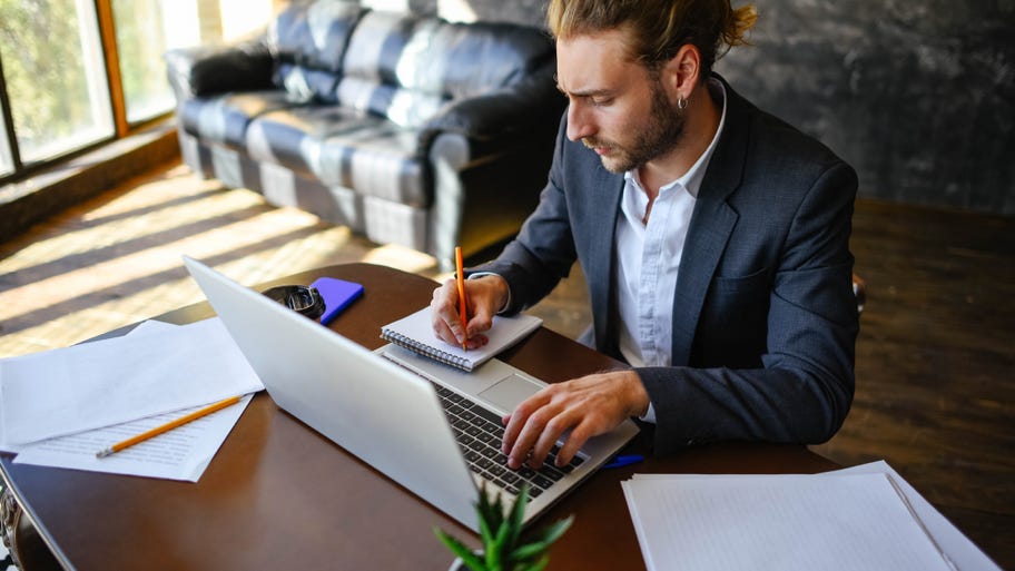 A young guy works at a laptop in a home office