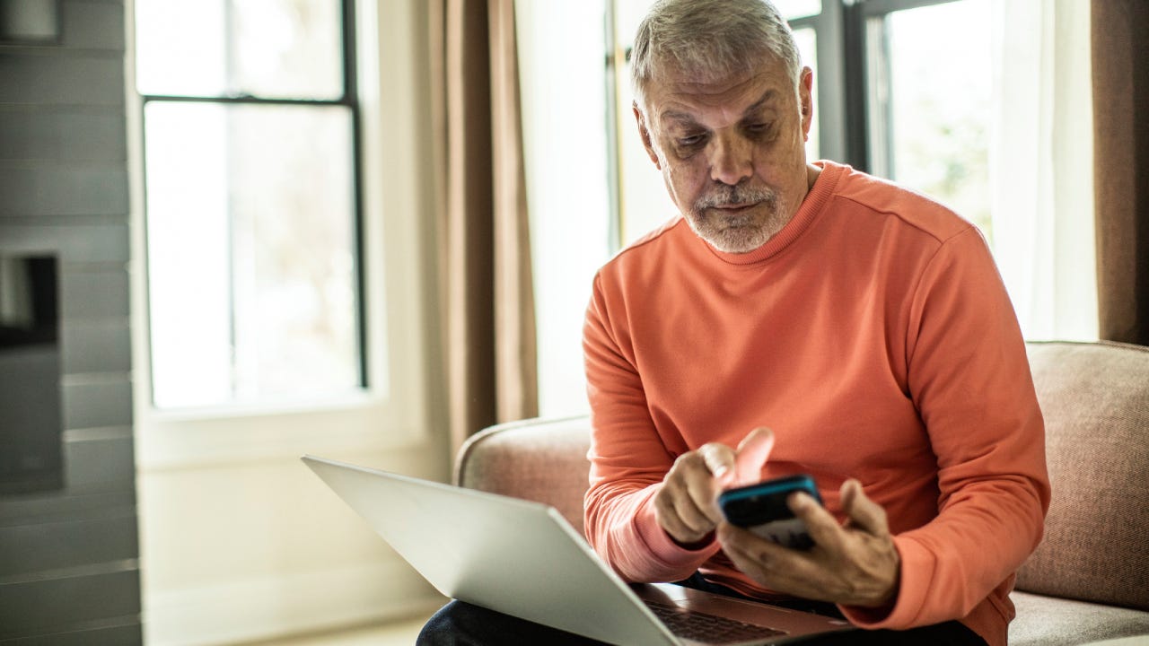 Senior man using laptop computer and smartphone at home