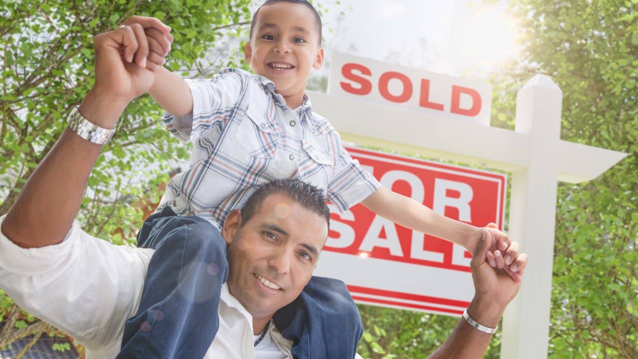 Hispanic father and son in front of a "Sold" real estate sign