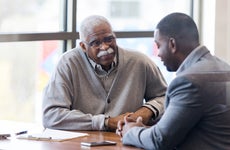 An older Black man talks with a Black loan officer at a credit union.