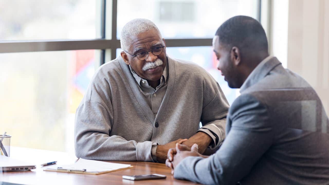 An older Black man talks with a Black loan officer at a credit union.