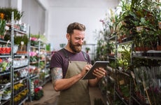 A florist stands in his nursery, looking at his tablet.