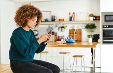 Woman using cell phone and sitting on kitchen counter