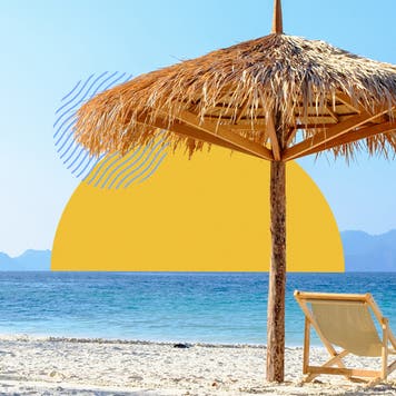 Scene of a beach with a woven grass umbrella over a nice beach chair in front of a clear, blue shoreline.