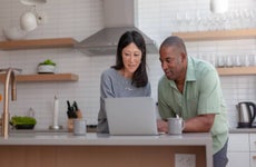 A mixed race couple use a laptop computer to pay bills online, manage budget and prepare tax documents. They are in the kitchen of their home.