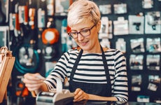 Smiling female business owner with short blonde hair and eyeglasses using cash register while standing in bicycle store.