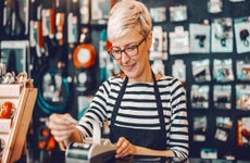 Smiling female business owner with short blonde hair and eyeglasses using cash register while standing in bicycle store.