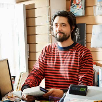 A bookshop owner stands behind his counter.