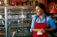 A Hispanic woman grins in a colorful bakery.
