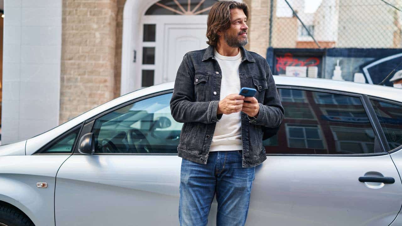 Middle age man using smartphone leaning on car at street