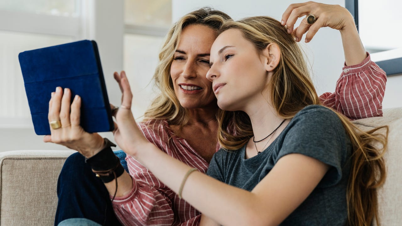 Smiling mother and daughter using digital tablet while sitting on sofa at home