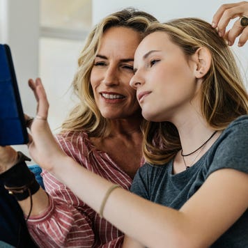 Smiling mother and daughter using digital tablet while sitting on sofa at home