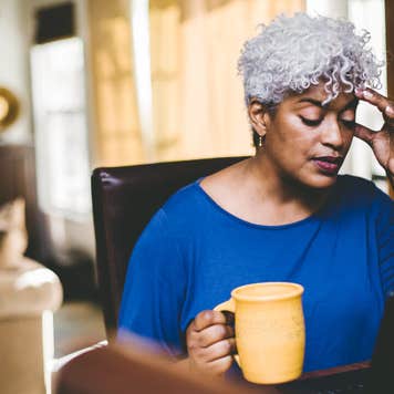 A woman with white hair puts a hand to her forehead while focusing on a computer screen.