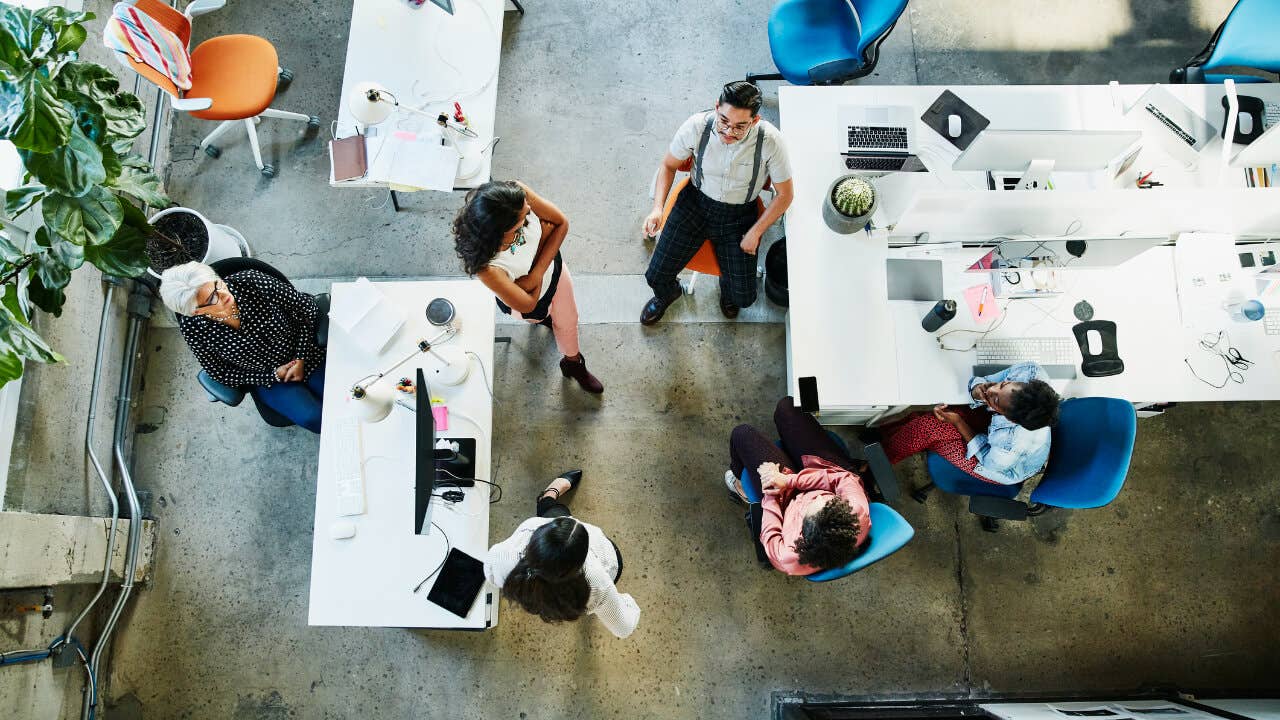 An overhead view of seated employees chatting in an open-plan office
