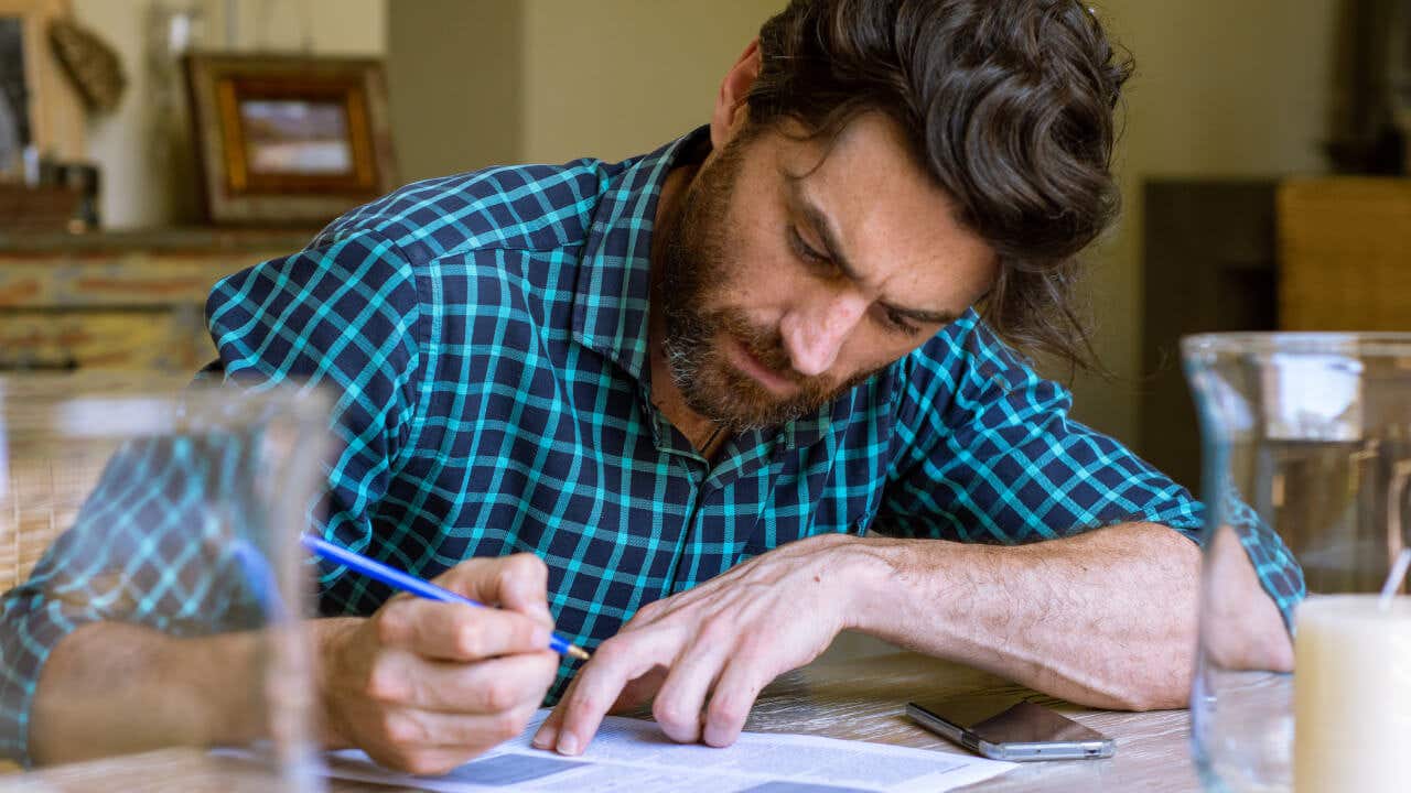 A bearded man concentrates on filling out a paper form.