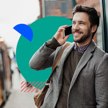 Man in a suit leans against a building, smiling and talking on his phone.