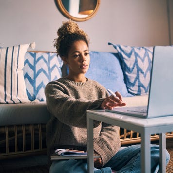 A freelancer sits on the floor in her living room, looking at her laptop.