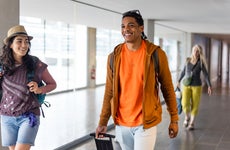 Friends walking through an airport together in Toulouse, France. They are heading to their departure area while carrying luggage and smiling.