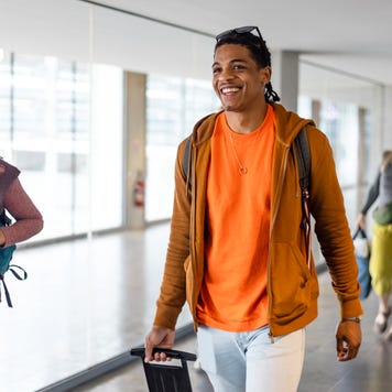 Friends walking through an airport together in Toulouse, France. They are heading to their departure area while carrying luggage and smiling.