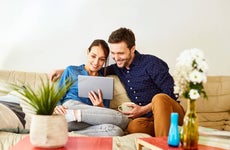 Mid adult couple using digital tablet on sofa. Relaxed man and woman are smiling while using internet. They are wearing casuals at home.