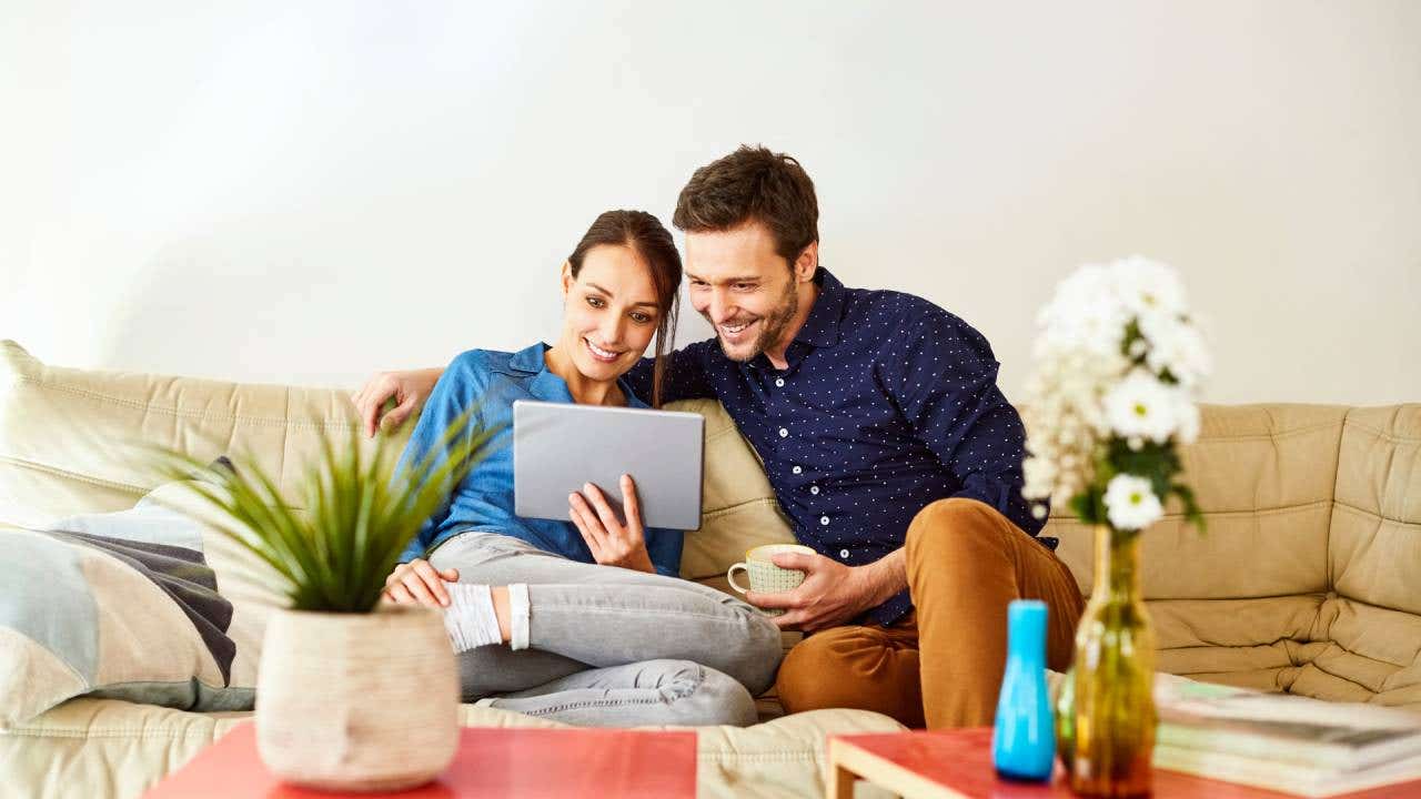 Mid adult couple using digital tablet on sofa. Relaxed man and woman are smiling while using internet. They are wearing casuals at home.