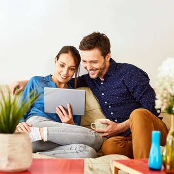 Mid adult couple using digital tablet on sofa. Relaxed man and woman are smiling while using internet. They are wearing casuals at home.