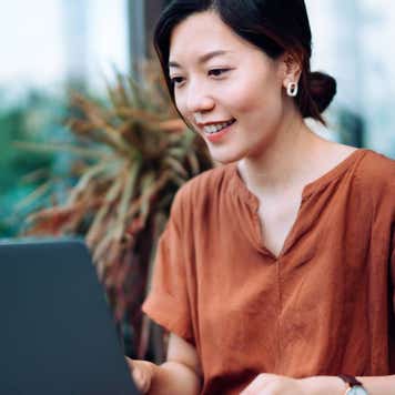 Young Asian woman using a laptop while seated on a balcony.