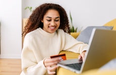 Smiling young ethnic woman holding credit card and using laptop computer at home. Online shopping concept