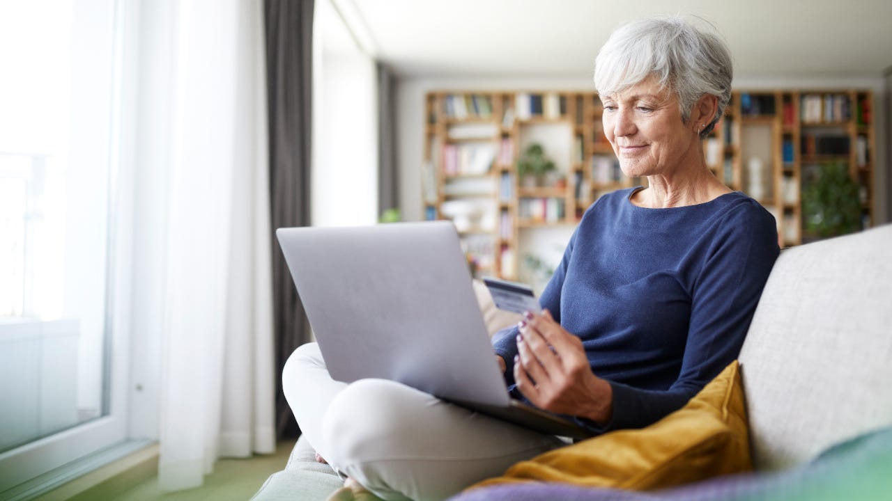 Senior woman using credit card while doing online shopping on laptop at home
