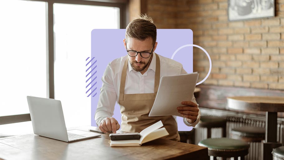 A business owner in an apron looks over paperwork