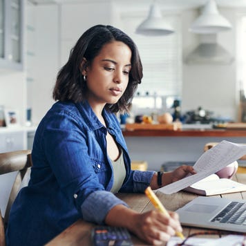 Shot of a young woman using a laptop and going through paperwork