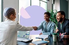 A Black business woman and her business partner shake hands across a table with another businessperson.