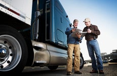 Two men look at paperwork next to a semi truck