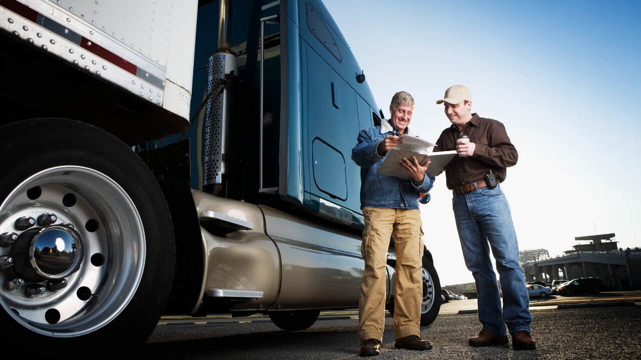 Two men look at paperwork next to a semi truck