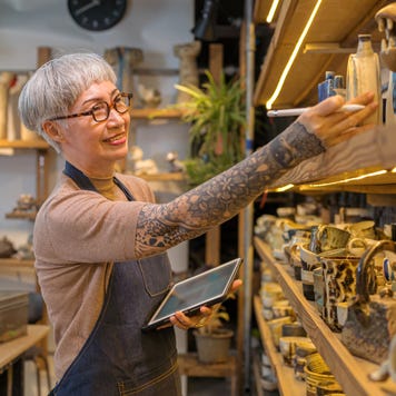 artist woman using digital tablet for stock counting on pottery shop