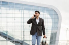 Indian business man walking outside to station or airport talking on the phone and carrying suitcase