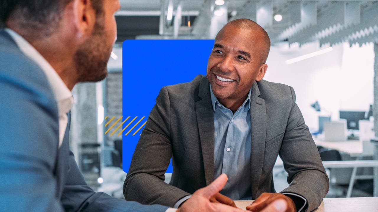 A smiling account sits with a client in his office.