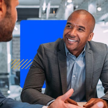 A smiling account sits with a client in his office.