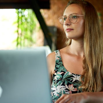 A young businesswoman sits in a cafe, looking up from her laptop