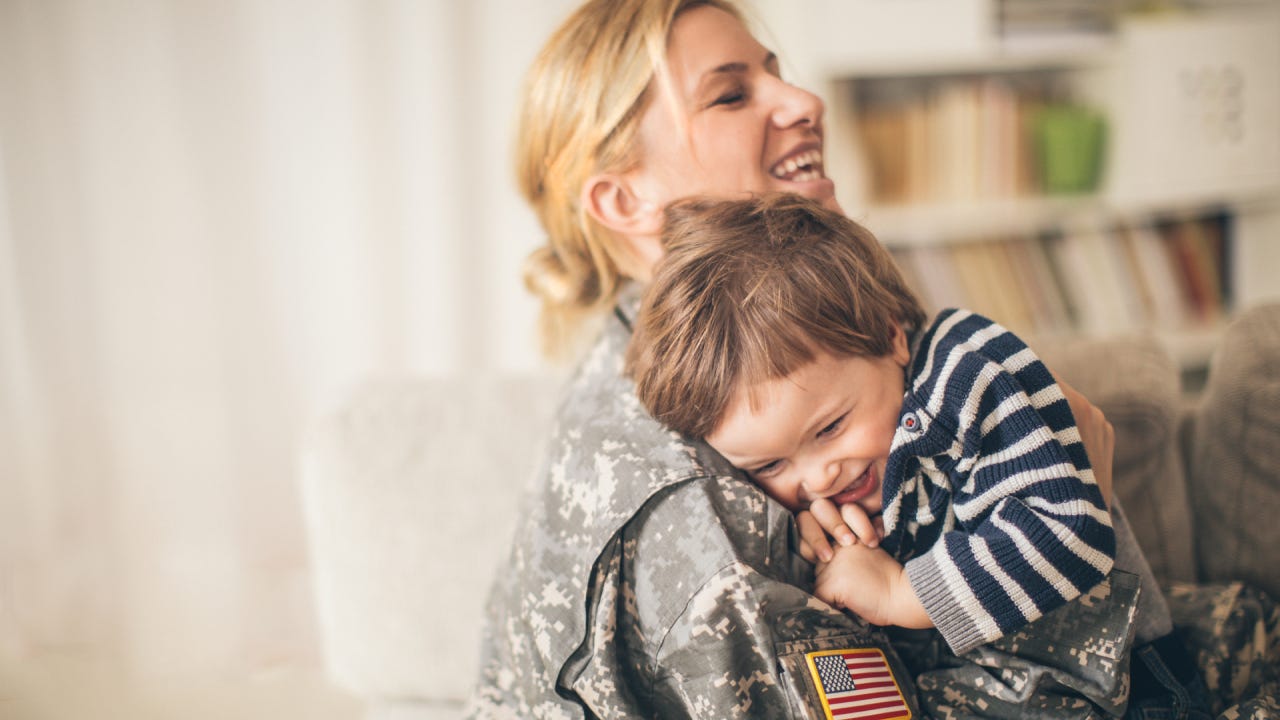 Photo of smiling young woman soldier and her son seeing after a long time and enjoying in their living room.
