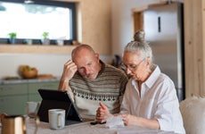 Senior couple sitting at the kitchen table looking at digital tablet and recalculating their expenses.